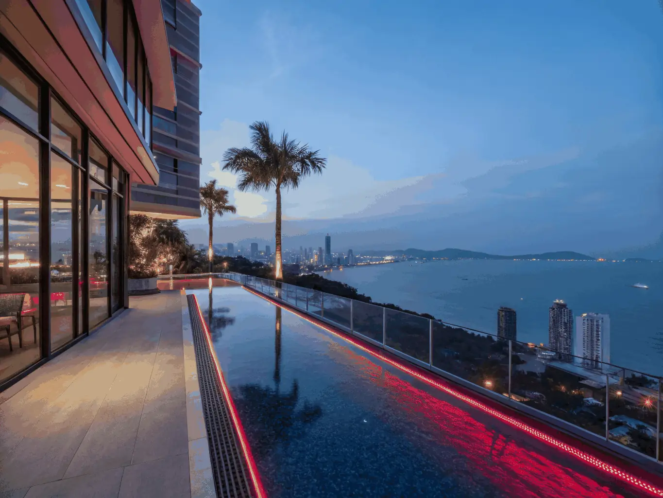 A high-angle shot of the Hilton Pattaya's infinity pool at sunset, overlooking Pattaya Bay, emphasizing luxury and exclusivity.